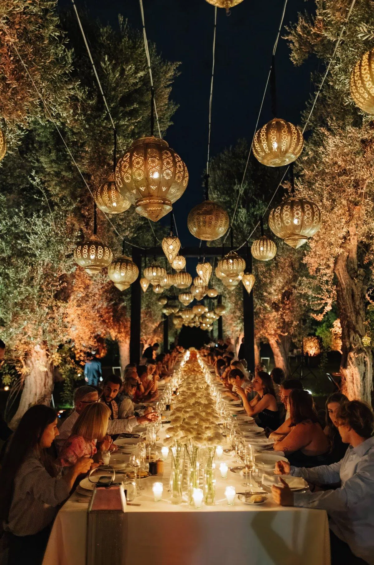 Longue table de réception sous des lanternes marocaines dans un jardin illuminé