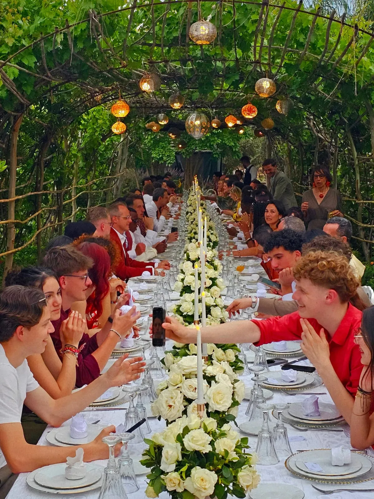 Longue table ornée de roses blanches et de bougies sous une pergola végétale